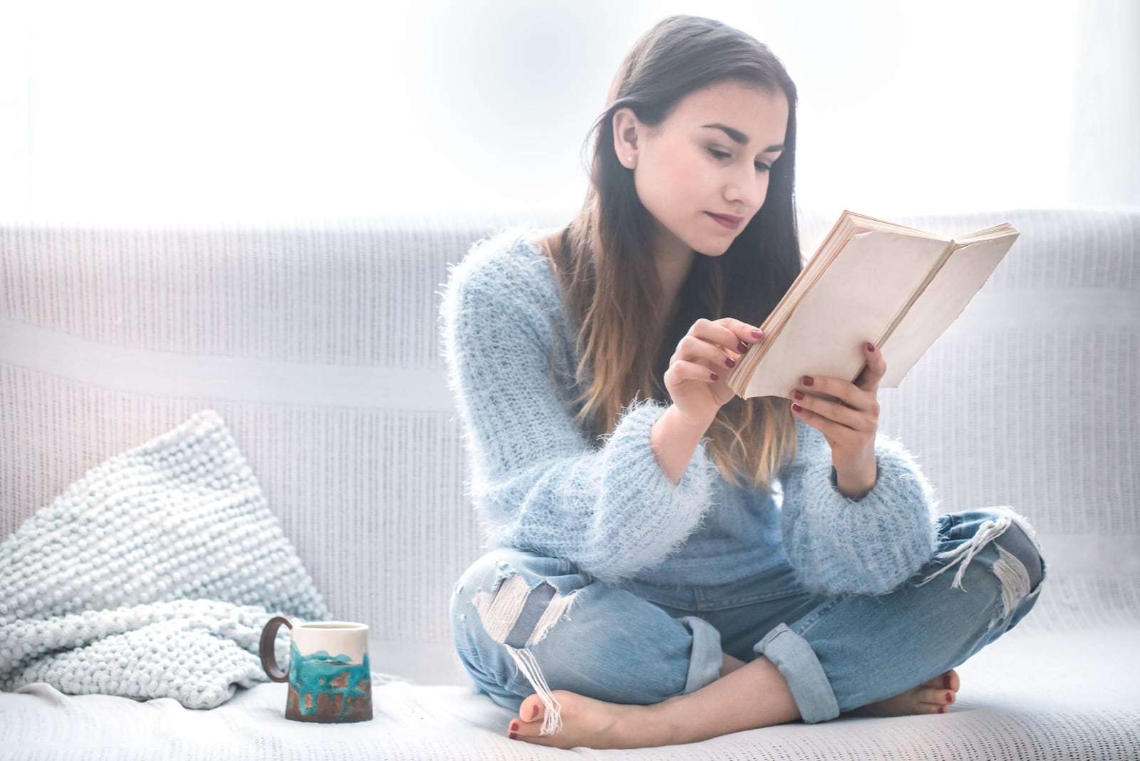 la donna è seduta sul divano a bere caffè e a leggere un libro