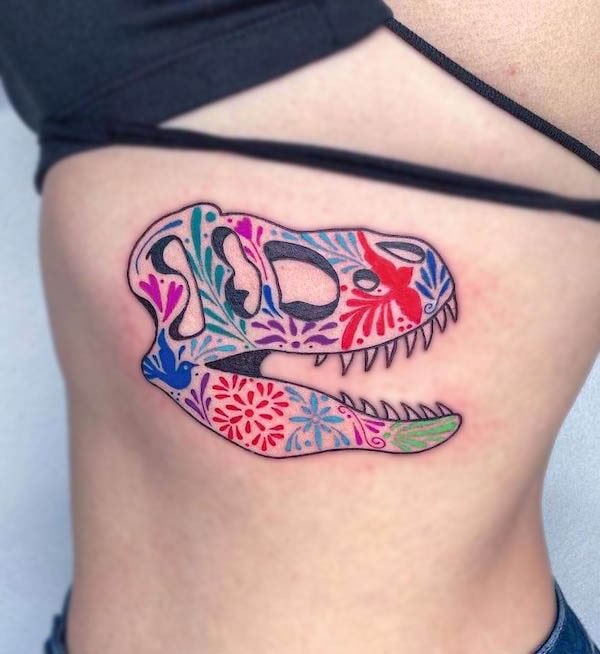 Tatuaggio del teschio di T-rex con motivi floreali colorati di @kareninjatattoo