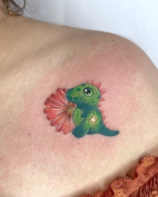 Baby dinosauro e fiore tatuato sulla spalla da @azu.tattoo