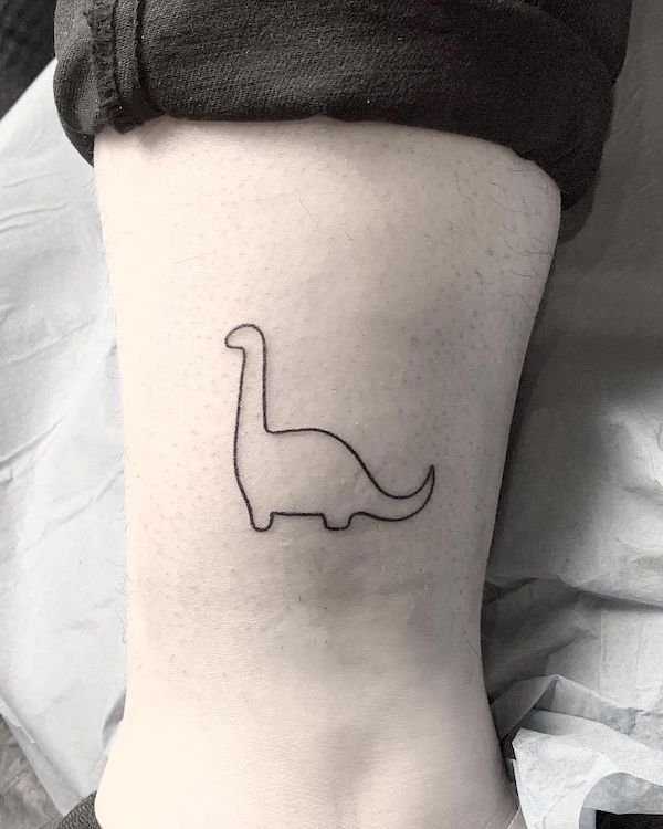 Piccolo dinosauro minimalista tatuato sopra la caviglia da @alekstattooer
